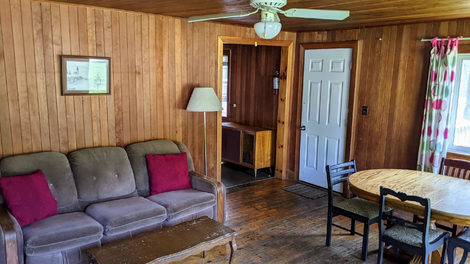 Pigeon Lake Resort Cottage Six.&nbsp; Cottage living room with wood-paneled walls, sofa, coffee table, dining table, and ceiling fan.